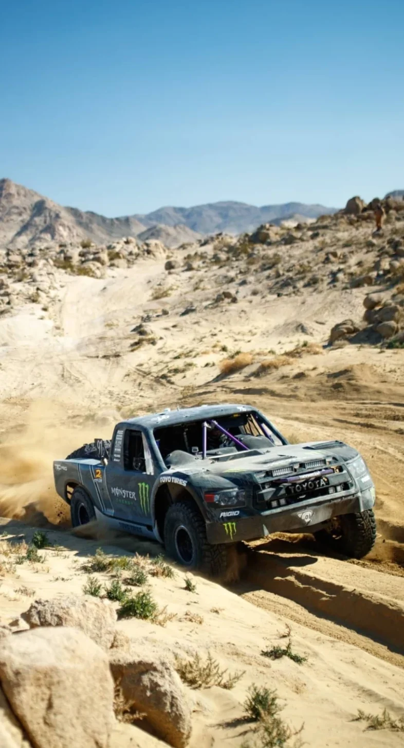 Trophy truck climbing through desert rocks and dust
